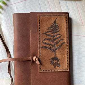 Handmade Leather Journal - guest book, blank journal, nature journal, book journal, gratitude journal - closeup view of the front cover with a stamped fern on suede hand-stitched to the leather cover. A leather thong is attached for tying the journal when not in use.