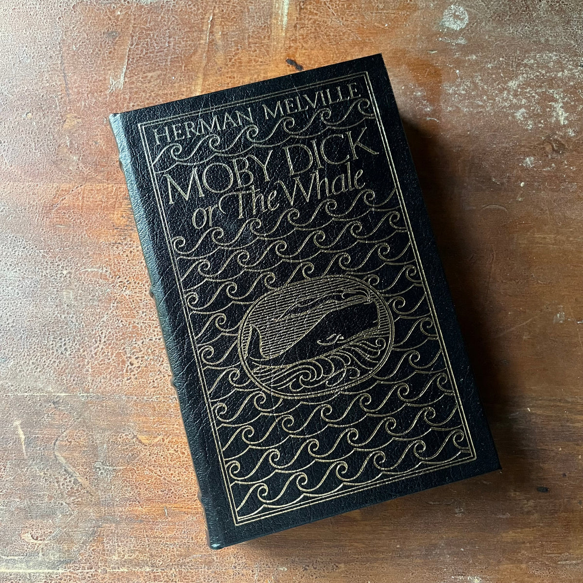 vintage children's chapter book, classic literature, gift book by Easton Press - Moby Dick or The Whale written by Herman Melville with illustrations by Broadhead Robinson - view of the embossed front cover in blue & gold - author & title listed along with waves & the whale in the middle of the cover