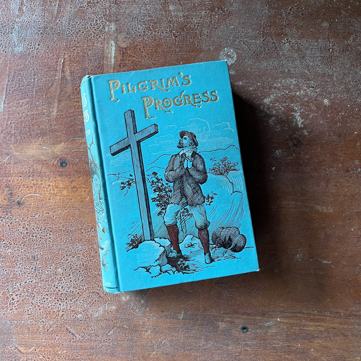 vintage religious tome, classic literature - Pilgrim's Progress written by Paul Bunyan also includes A Life of Bunyan by James Anthony Froude - view of the embossed front cover with an illustration of a man standing before a cross with his hands on his heart