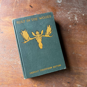 vintage children's chapter book, boy scout adventure book - Rolf in the Woods written & illustrated by Ernest Thompson Seton - view of the embossed, green front cover with a yellow moose head & writing in yellow (book title & author)