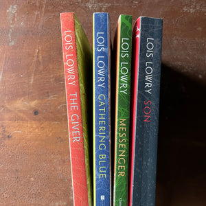 The Giver Quartet Book Set written by Lois Lowry-The Giver, Gathering Blue, Messenger, and Son-Newbery Award Winning Book-Dystopian Young Adult Science Fiction-view of the spines in red, blue, green & black with white writing of Author's name & the title of the book plus publisher