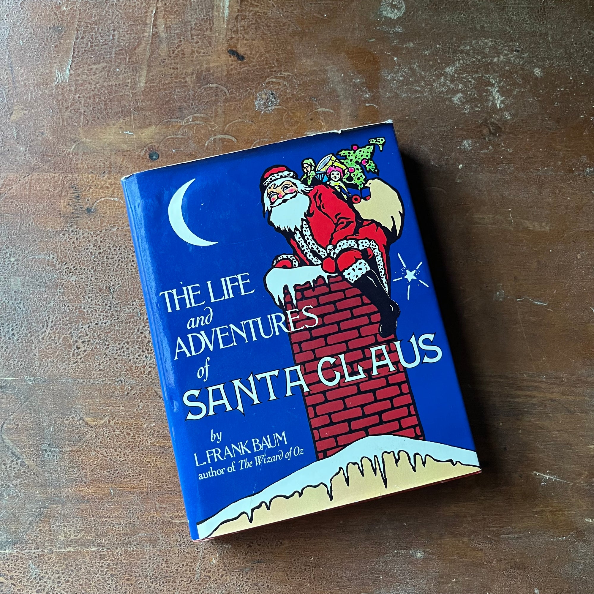 vintage children's chapter book - The Life & Adventures of Santa Claus written by L. Frank Baum with illustrations by Mary Cowles Clark - view of the dust jacket's front cover with an illustration of Santa on top of a chimney