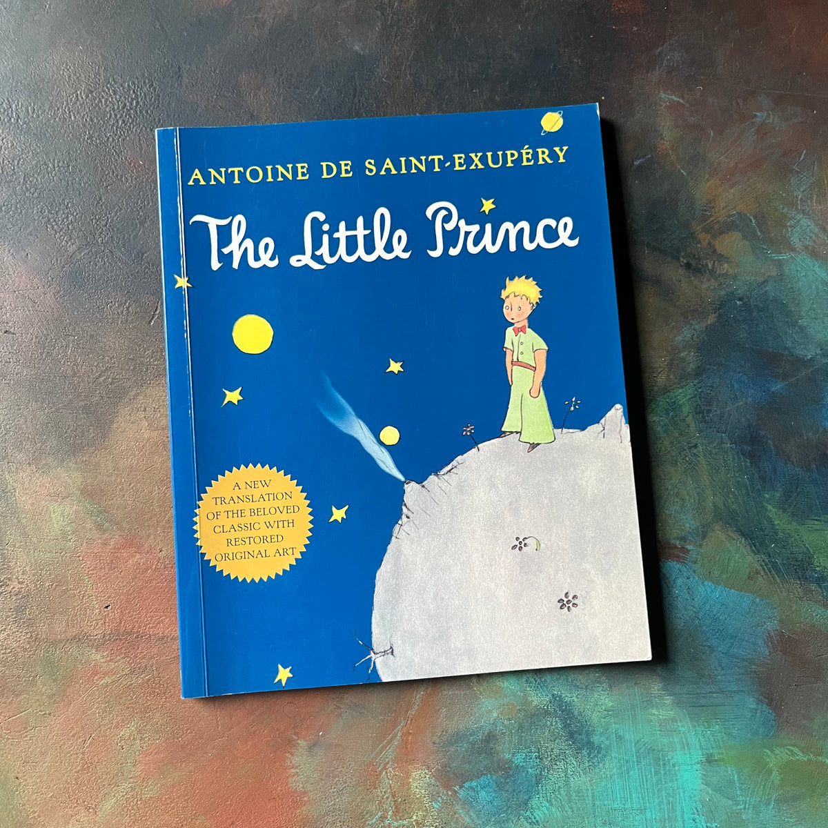 Antoine De Saint-Exupery's The Little Prince-classic children's literature-view of the front cover with a blue background & an illustration of the little prince on a planet