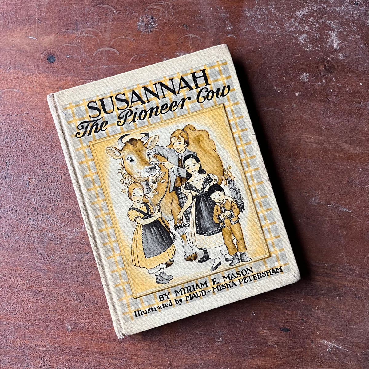 Log Cabin Vintage – vintage children’s book, children’s book, chapter book - Susannah The Pioneer Cow written by Mariam E. Mason with illustrations by Maud and Miska Petersham - view of the book sitting on an old wood table showing the front cover