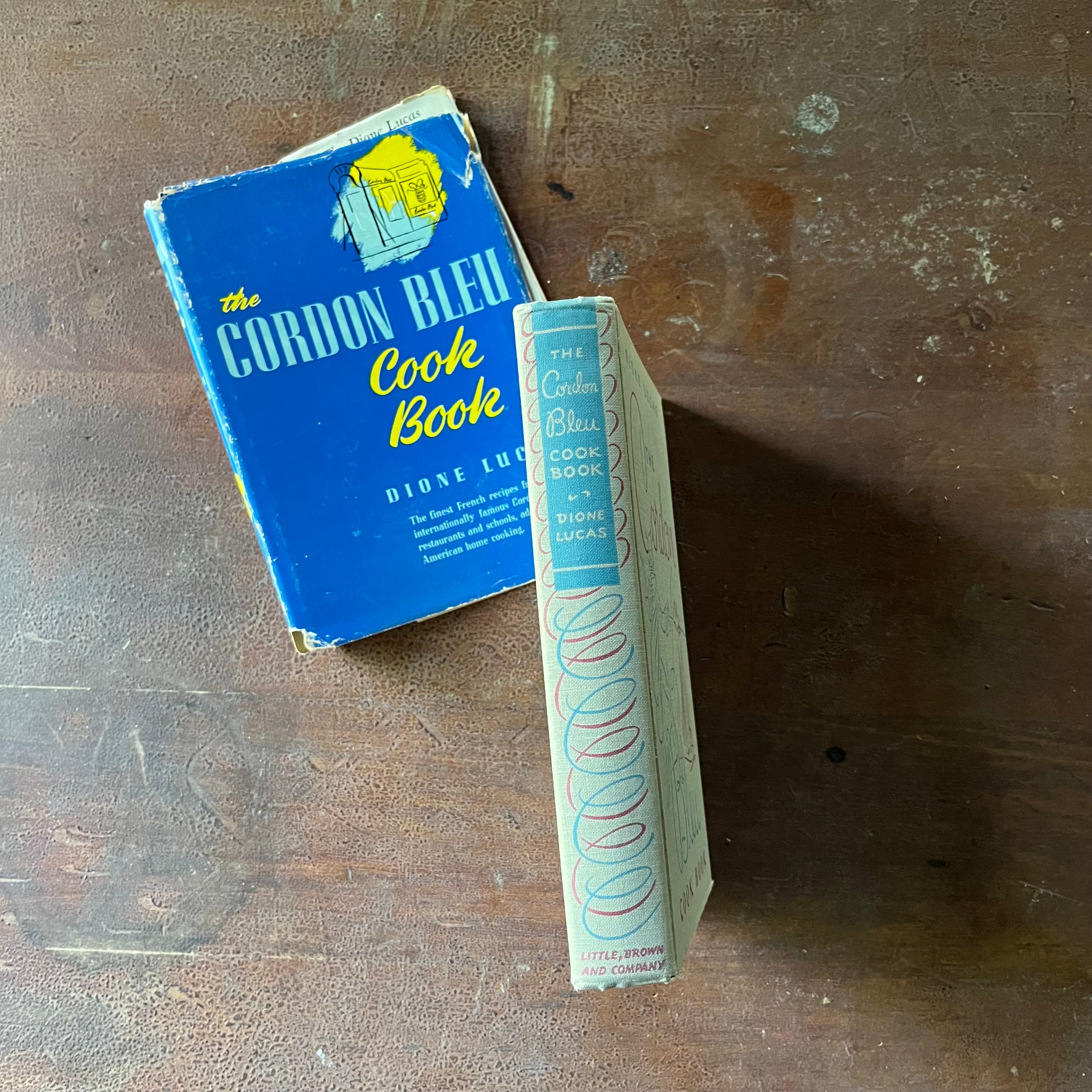 The Cordon Bleu Cook Book by Dione Lucas - spine of the book  & dust jacket shown displayed on a wood table