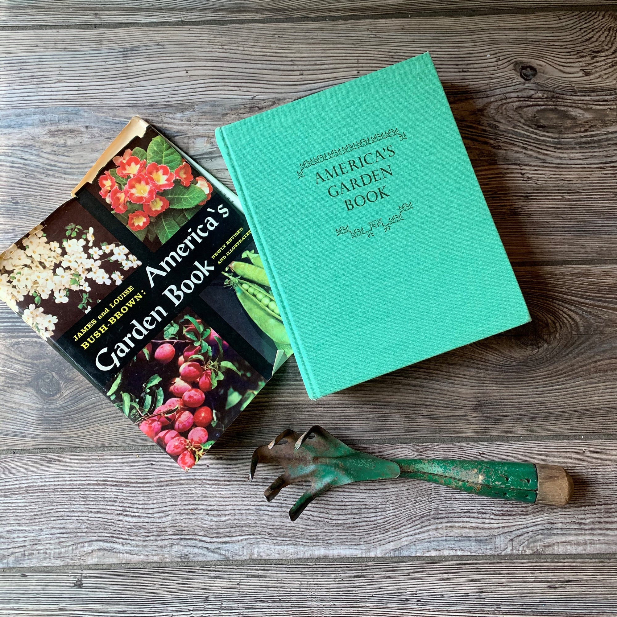 Log Cabin Vintage - vintage non-fiction book, vintage gardening book, American Gardening, Garden Book - America's Garden By Louise and James Bush-Brown 1967 Edition - view of the front cover with the dust jacket & a gardening tool all sitting on a wood table