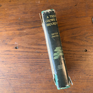 Log Cabin Vintage - vintage fiction, American Author, American novel - A Tree Grows in Brooklyn by Betty Smith - view of the book on a wood table showing the dust jacket's spine